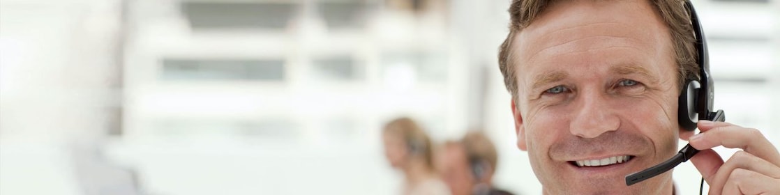 A man wearing a headset and having a phone call. Two more people in the background doing the same - blurred out.
