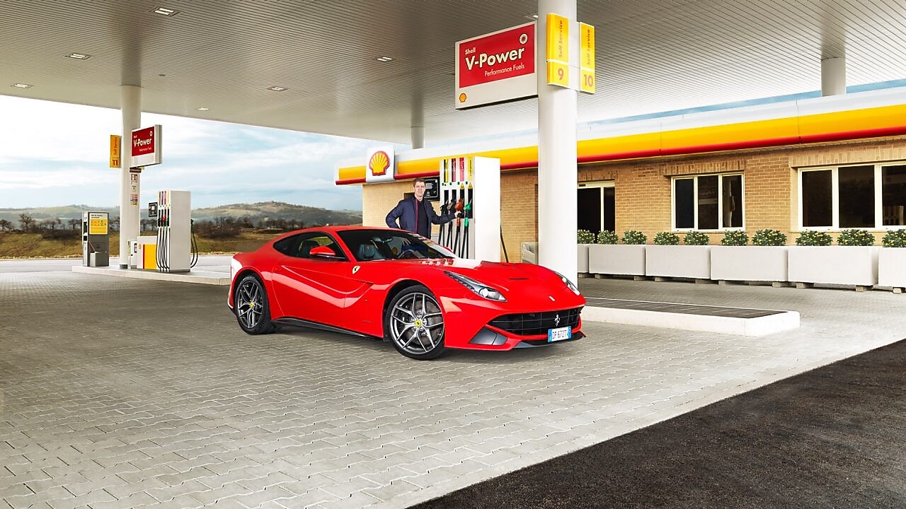 Une Ferrari rouge arrêtée à la pompe d'une station Shell avec un homme qui s'apprête à faire le plein